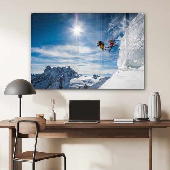 Twee skiërs springen van een berg, met de zon fel schijnend in de blauwe lucht.