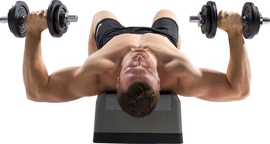 Man ligt op zijn rug op een bankje en doet oefeningen met dumbbells.