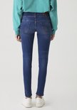 Achterkant van een model met een turquoise trui en witte sneakers, draagt een donkerblauwe, nauwsluitende jeans.