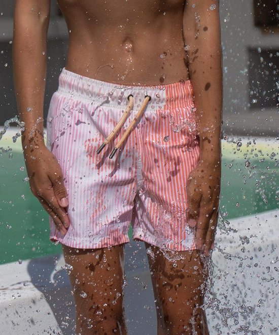 Zwemshort met verticale oranje-witte strepen en verfspatten, omringd door water.