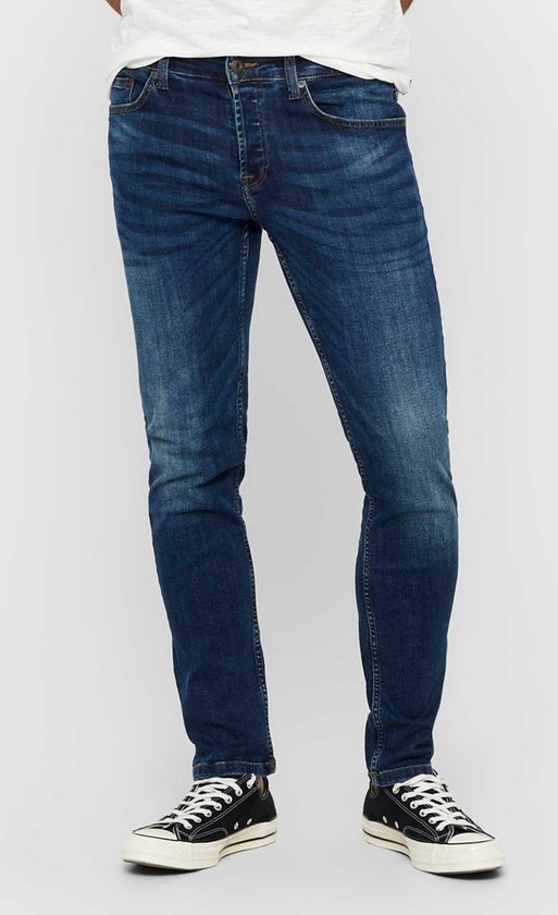 Man in een strakke, donkerblauwe jeans met lichte wassing en verfspatten.