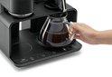 Een hand pakt een glazen koffiekan uit een zwart koffiezetapparaat met digitaal bedieningspaneel.