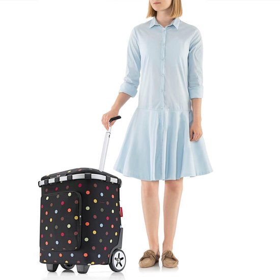 Vrouw in lichtblauwe jurk met boodschappentrolley met veelkleurige stippen en wielen.