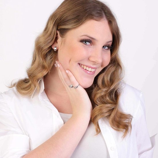 Glimlachende vrouw met blonde krullen, draagt zilverkleurige ring en oorbellen. Hand met ring bij de kin.