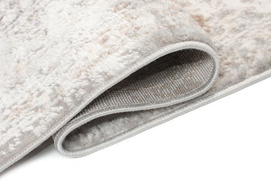 Un tapis beige enroulé montre la texture douce et le dos brun avec une couture grise.