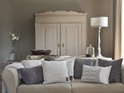 Een comfortabele beige bank vol met diverse gebreide sierkussens in grijstinten en off-white, met een gebreide plaid.