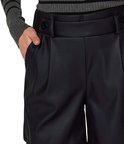 Close-up van een vrouw in zwarte faux leren shorts met strikdetail op de tailleband en zwarte knopen.