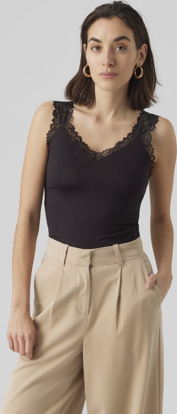 Model met donkerbruin haar en gouden oorbellen draagt een zwarte tanktop met kanten rand en beige wijde broek.