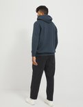 Man met donkere huid staat met de rug naar de camera, draagt een donkerblauwe hoodie en zwarte jeans.