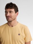 Man met licht getinte huid draagt een donkergeel T-shirt met een klein rond logo met 'P' op de linkerborst.