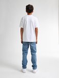 Achterkant van een jongen in een wit t-shirt en een lichte, rechte spijkerbroek.