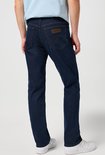 Man in donkerblauwe Wrangler jeans met een blauw shirt, achterkant.