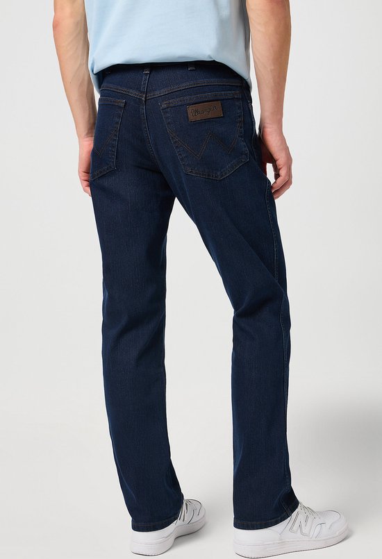 Man in donkerblauwe Wrangler jeans met een blauw shirt, achterkant.