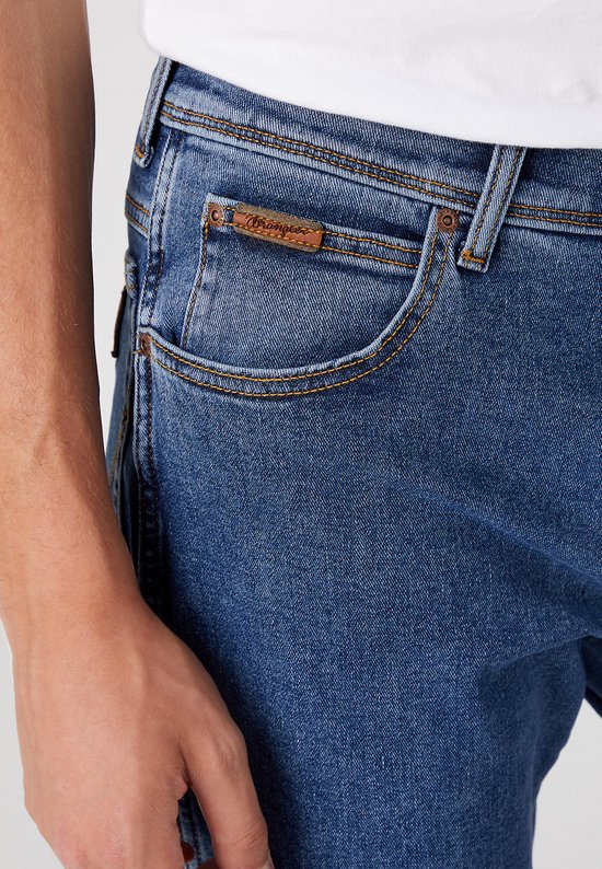 Detail van blauwe Wrangler jeans met bruin label op de zak.