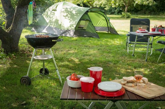 Een campingopstelling met een tent, grill, tafel met eten en stoelen.