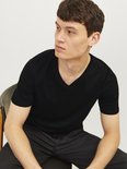 Man met zwart V-hals T-shirt en zwarte broek, zittend.