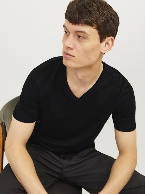 Man met zwart V-hals T-shirt en zwarte broek, zittend.