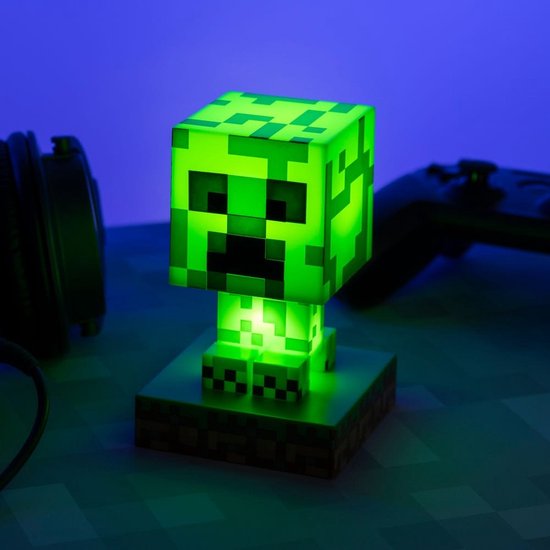 Een felgroene Minecraft Creeper-lamp, gloeiend met intern licht, staand op een gras- en aarde-voetstuk.