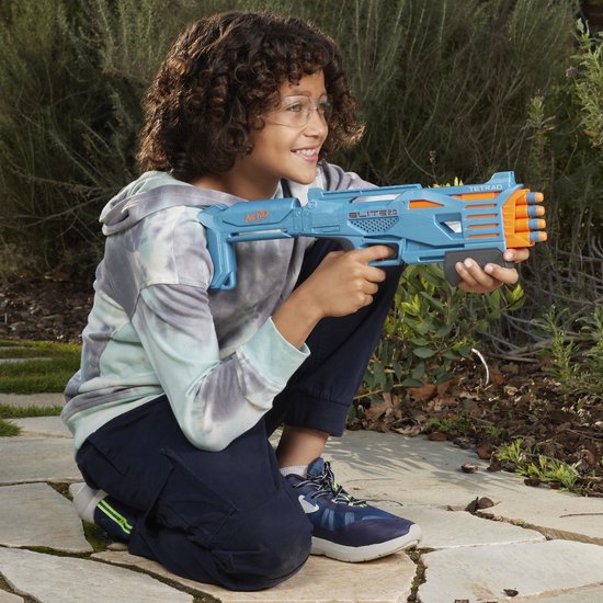 Jongen met veiligheidsbril knielt en houdt een blauwe Nerf Elite Tetrad blaster vast.