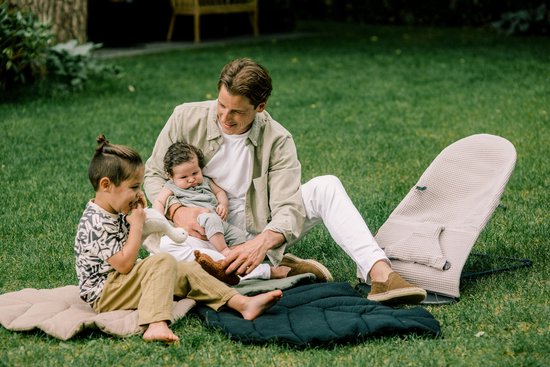 Man zit in het gras met twee kinderen en een beige wipstoel.