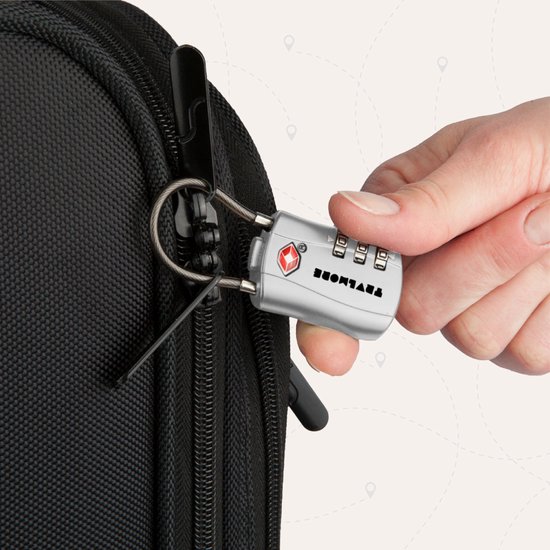Hand sluit een zilverkleurig TRVLMORE kofferslot met 3 cijfers aan op een rits van een zwarte reistas.