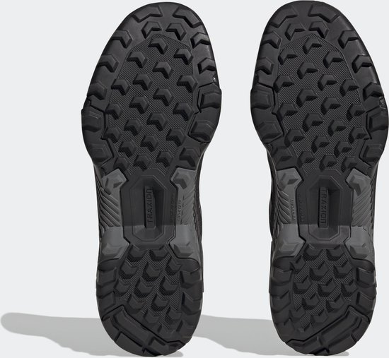 De onderkanten van twee zwarte wandelschoenen met een robuust profiel en 'TRAXION' op de zool.