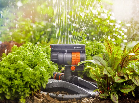 Arroseur oscillant GARDENA compact dans un jardin verdoyant avec des jets d'eau.
