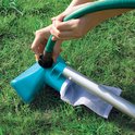 Handen sluiten een tuinslang aan op een turquoise schepnet met een zilveren steel en een wit gaaszakje op groen gras.