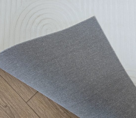 Detail van de onderkant van een crème laagpolig vloerkleed met gebogen lijnen en een grijze achterkant.