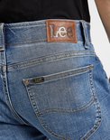 Close-up van de achterkant van een lichtblauwe jeans met Lee-logo op de leren patch en op een klein label.