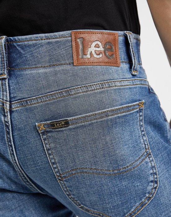 Close-up van de achterkant van een lichtblauwe jeans met Lee-logo op de leren patch en op een klein label.