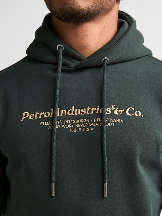 Detailopname van de donkergroene hoodie met gouden tekstprint.