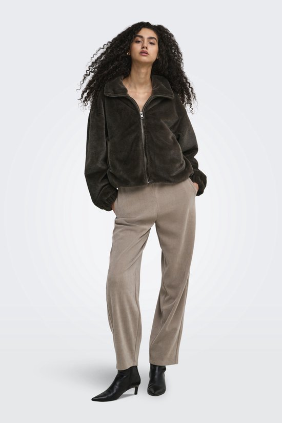 Model met krullend haar draagt een donkerbruine teddy jas met ritssluiting en een beige corduroy broek.