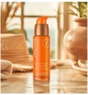 Lancaster Golden Tan Maximizer flacon met oranje pompdispenser, omringd door strandattributen.