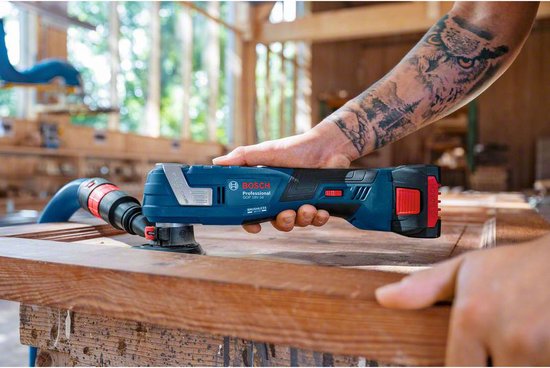 Blauwe en zwarte Bosch Professional multitool in handen van persoon met tatoeage op arm, aan het werk op hout.