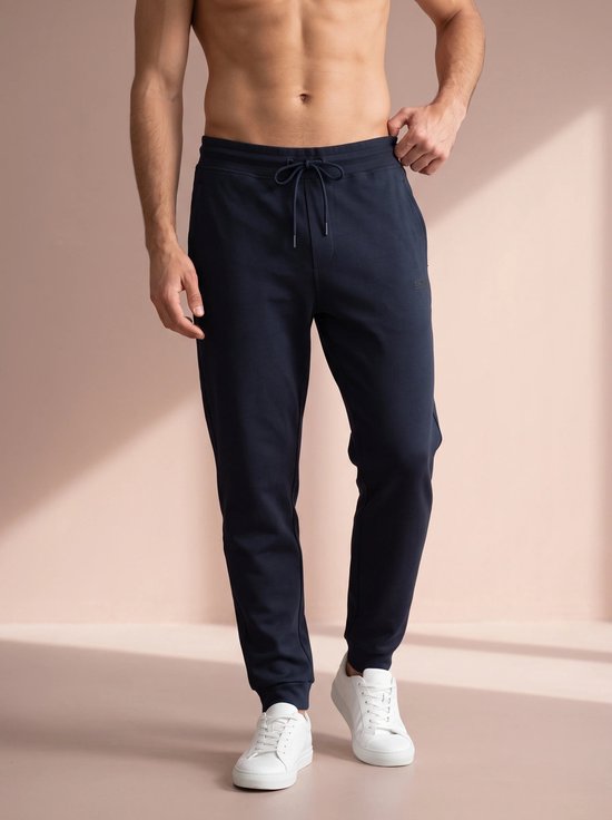 Man in donkerblauwe joggingbroek met trekkoord en witte sneakers.