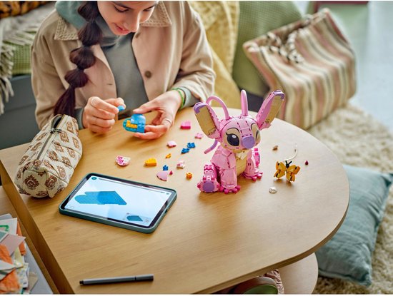 Fille construisant avec LEGO Disney Angel et papillon. Table remplie de pièces LEGO et tablette avec instructions.