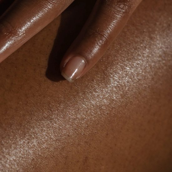 Close-up van een donkere huid met glanzende olie en een nagel.