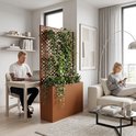 Een bruine plantenbak met planten als roomdeler in een woonkamer.
