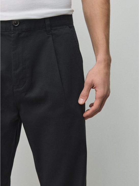 Close-up van de taille en heup van een zwarte chino met taps toelopende pasvorm op een model.