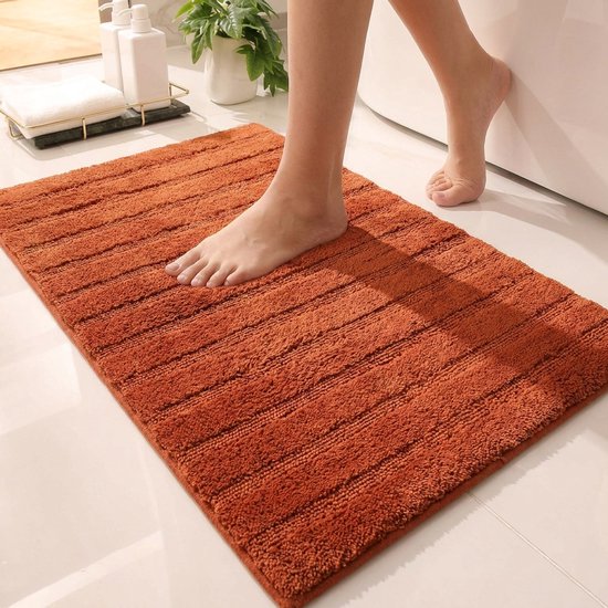 Voet op een oranje badmat met ribbels, naast een bad.