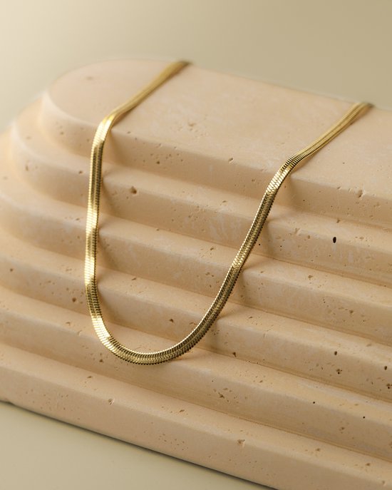 Gouden slangenketting liggend op een beige, gestructureerde display met lagen.