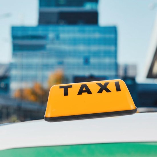 Oranje taxibord met zwarte letters 'TAXI' op een dak, stadsachtergrond.