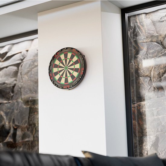 Rood dartbord met groen, zwart en wit op een witte muur in een kamer met stenen muur.