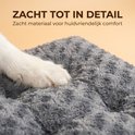 Close-up van een poot van een witte hond op een zacht, grijs, fluffy hondenkussen.
