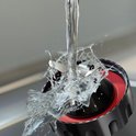 Water stroomt op de messen van een zwarte blender met rode ring, roestvrij staal.