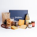 Een Zuivelhoeve borrelpakket met kaas, worst, pretzels, nootjes, sap en jam in een blauwe doos.