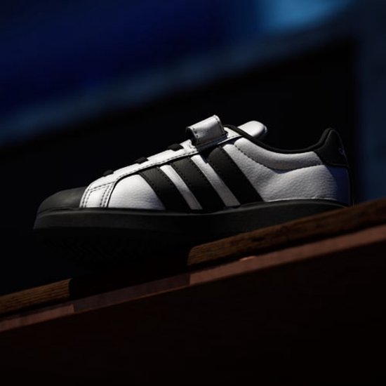 Wit Adidas kindersneaker met zwarte strepen en klittenbandsluiting.