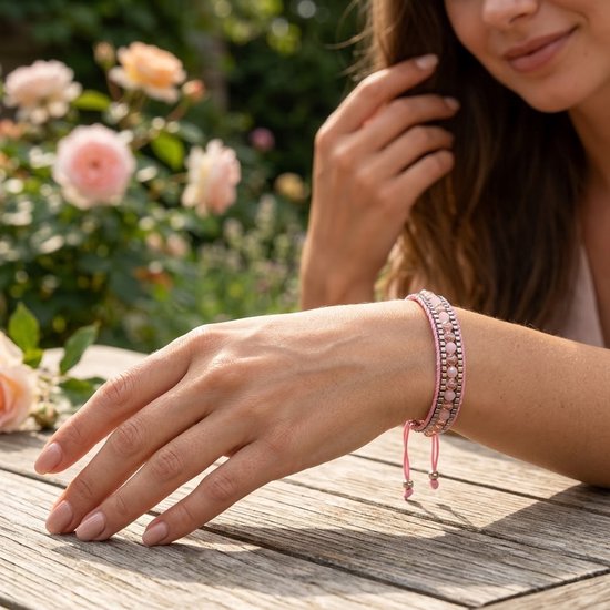 Model draagt een roze geweven armband met facet geslepen glaskralen, aan een verstelbaar koord, in een tuin.