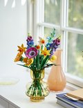 Een vaas met LEGO wilde bloemen, waaronder gele leeuwenbekjes, paarse lupines en blauwe korenbloemen.